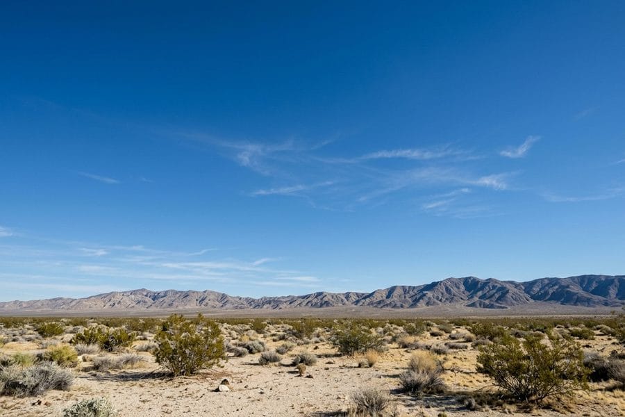 Wide blue sky over open High Desert scrubland and a distant bare mountain range near Hesperia