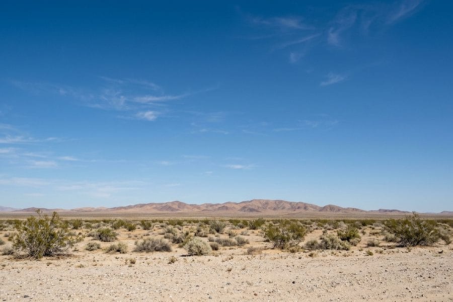 Flat open Colorado Desert scrubland with a distant low range under a wide clear blue sky in eastern Riverside County